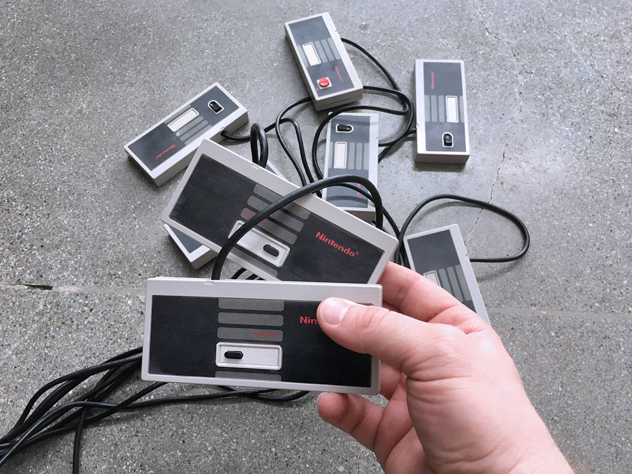 A photograph of a hand holding the START and SELECT controllers with the other six in the background.